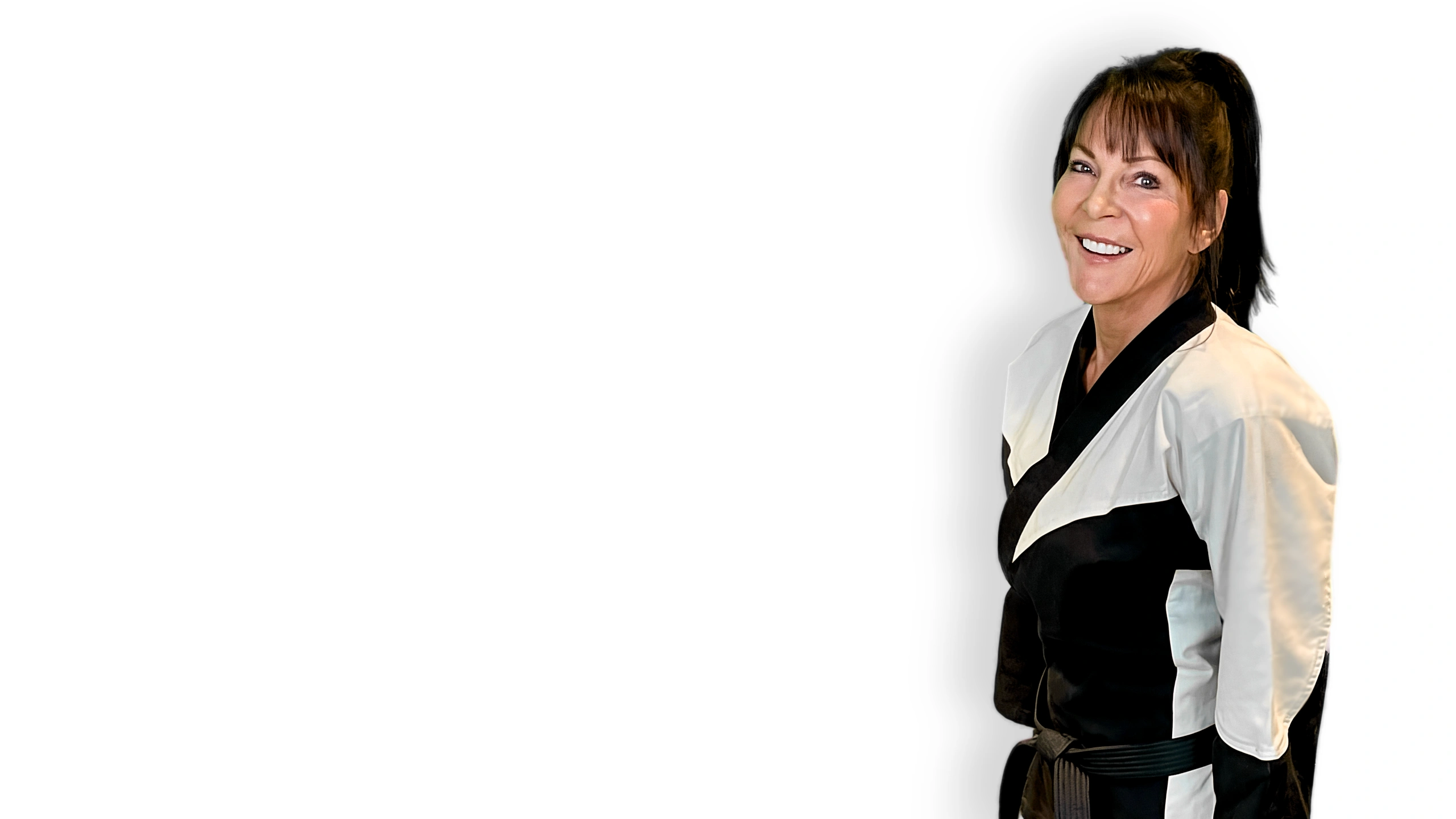 Jan, a smiling woman in a black and white karate uniform, stands confidently against a clean white background.