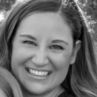 A black and white close-up portrait of Katherine Horning smiling broadly. She is looking directly at the camera with a warm, friendly expression.
