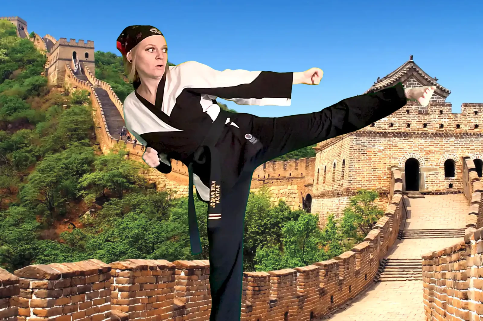 Karate instructor Katie, wearing a black gi and bandana, executes a powerful side-kick with a focused expression, against the backdrop of the Great Wall of China.