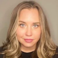 A close-up portrait of Alyssa R., a woman with wavy blonde hair and light eyes, wearing a black shirt and looking directly at the camera.
