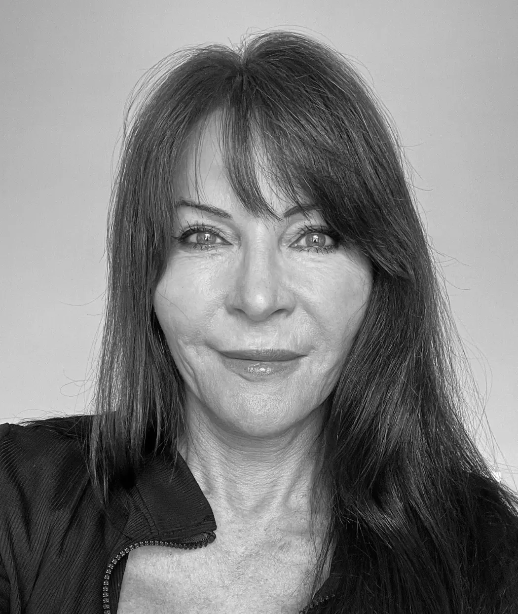 A black and white headshot of author Jan Stockton with long dark hair, wearing a black zipped jacket and smiling slightly.