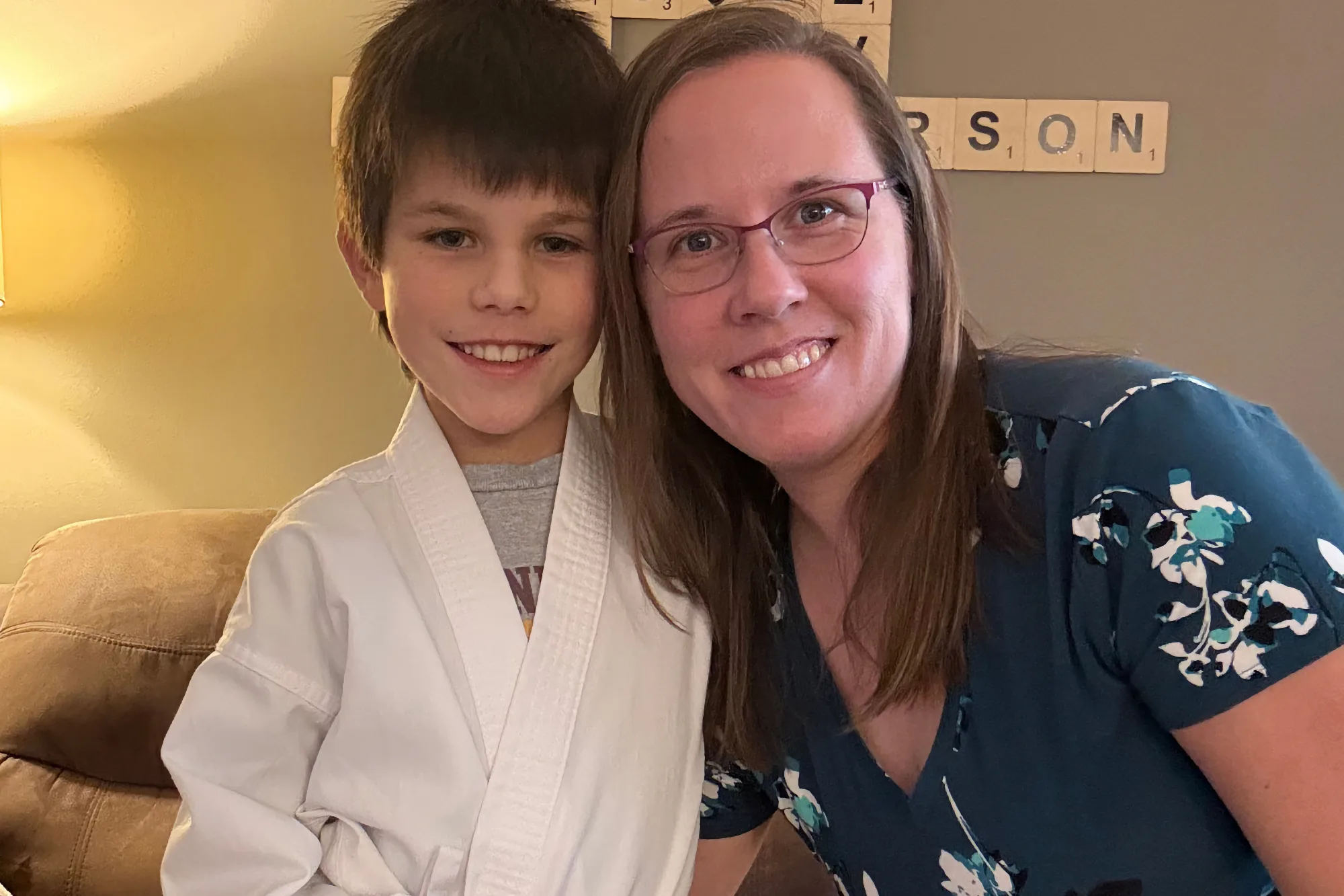 Mom and a young boy in a white karate gi smile brightly together for a close-up family photo.